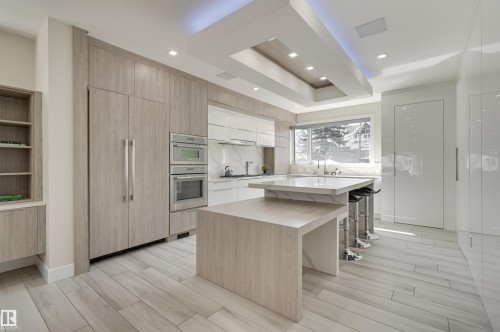 Contemporary kitchen featuring a multi-tiered island with integrated seating, stainless steel double ovens, and a built-in paneled refrigerator - 9741 90 Avenue, Edmonton, AB - Indoor