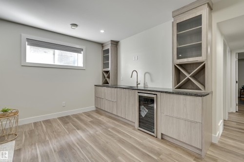 Wet bar featuring light wood-finish cabinetry, a dark countertop, an integrated sink with a gooseneck faucet, a built-in beverage refrigerator, and wine storage - 9741 90 Avenue, Edmonton, AB - Indoor
