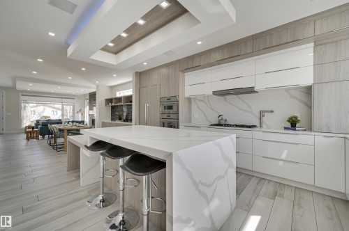 Gourmet kitchen with a large central island, light wood-finish flooring, integrated appliances, white flat-panel cabinetry, and a matching stone backsplash - 9741 90 Avenue, Edmonton, AB - Indoor Photo Showing Kitchen With Upgraded Kitchen