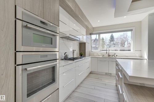 Modern kitchen featuring integrated stainless steel appliances, wood-finish flooring, and white cabinetry - 9741 90 Avenue, Edmonton, AB - Indoor Photo Showing Kitchen