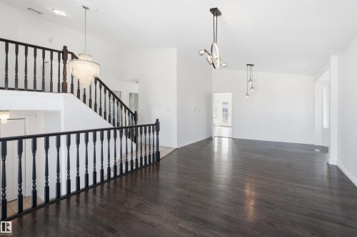 Expansive interior showcasing dark hardwood flooring, a prominent staircase with dark balusters, and contemporary lighting fixtures - 6009 36 Avenue, Beaumont, AB - Indoor Photo Showing Other Room