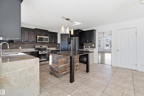 The kitchen features dark cabinetry, stainless steel appliances, and a stone-clad island - 6009 36 Avenue, Beaumont, AB - Indoor Photo Showing Kitchen