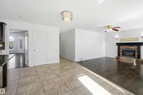 Spacious living area featuring dark hardwood flooring, a stone fireplace with a dark mantel, and an overhead ceiling fan - 6009 36 Avenue, Beaumont, AB - Indoor With Fireplace