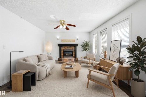Bright living area featuring a fireplace with a stone surround and mantel, a ceiling fan, and large windows providing natural light - 6009 36 Avenue, Beaumont, AB - Indoor Photo Showing Living Room With Fireplace