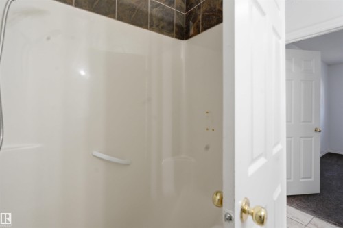 The bathroom features a shower with an integrated grab bar and tiled surround - 6009 36 Avenue, Beaumont, AB - Indoor Photo Showing Bathroom