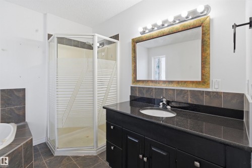 Well-appointed bathroom featuring a dark granite countertop vanity with an integrated sink and a framed mirror - 6009 36 Avenue, Beaumont, AB - Indoor Photo Showing Bathroom