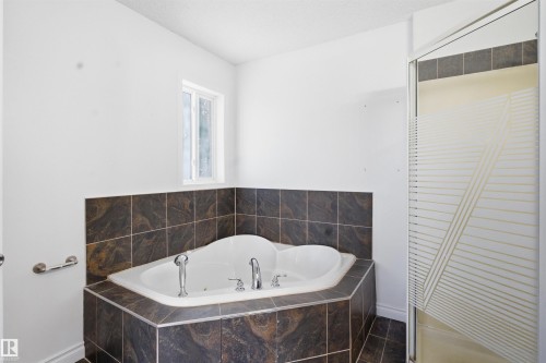 Bathroom featuring a corner bathtub with chrome fixtures, surrounded by dark tiled walls and flooring - 6009 36 Avenue, Beaumont, AB - Indoor Photo Showing Bathroom
