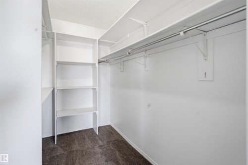 Spacious walk-in closet featuring white built-in shelving and hanging rods, complemented by carpeted flooring - 6009 36 Avenue, Beaumont, AB - Indoor With Storage