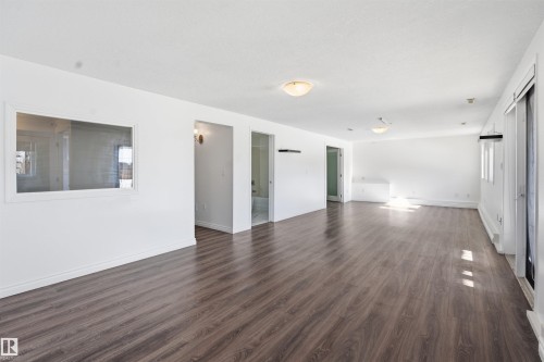 This expansive interior space features dark wood-look flooring and white walls, creating a bright and open atmosphere - 6009 36 Avenue, Beaumont, AB - Indoor Photo Showing Other Room