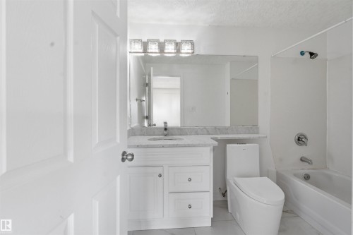 The bathroom features a white vanity with a light-colored countertop, a large mirror, and a modern toilet - 6009 36 Avenue, Beaumont, AB - Indoor Photo Showing Bathroom