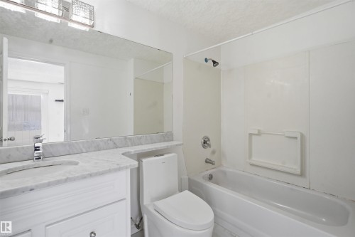 Bathroom featuring a white vanity with a marble countertop, a large mirror, and a full-size bathtub with an overhead shower - 6009 36 Avenue, Beaumont, AB - Indoor Photo Showing Bathroom