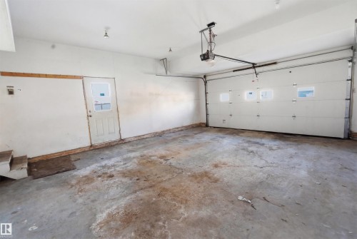 Spacious garage featuring a large overhead door with window inserts, an additional access door, and a concrete floor - 6009 36 Avenue, Beaumont, AB - Indoor Photo Showing Garage