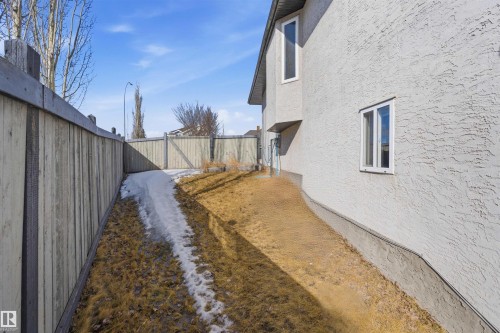 Side yard featuring a textured stucco exterior, white-framed windows, and a wood privacy fence - 6009 36 Avenue, Beaumont, AB - Outdoor