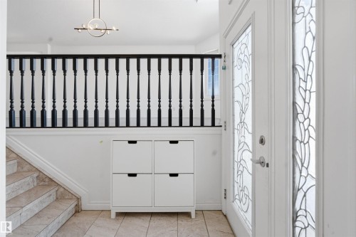 The entryway features a front door with decorative glass inserts, a tiled floor, and a staircase with a black balustrade - 6009 36 Avenue, Beaumont, AB - Indoor Photo Showing Other Room