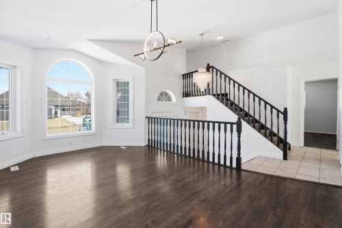 Spacious interior featuring dark hardwood floors, large arched windows, and a staircase with dark balusters - 6009 36 Avenue, Beaumont, AB - Indoor Photo Showing Other Room