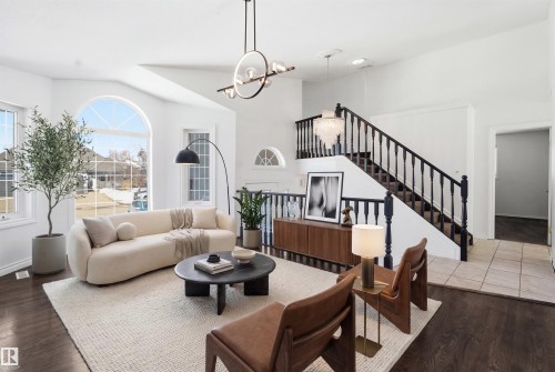 This living area features dark wood flooring, a staircase with dark wood banisters, and arched windows - 6009 36 Avenue, Beaumont, AB - Indoor Photo Showing Living Room