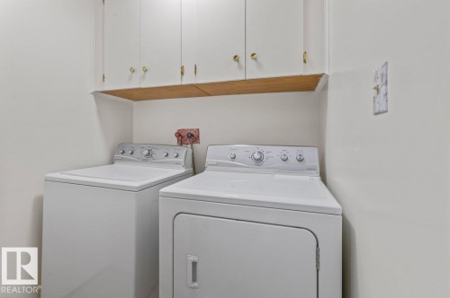Laundry area featuring white cabinetry with gold-tone hardware, a light wood-finish shelf, and neutral wall paint - 219 Knottwood Road N, Edmonton, AB - Indoor Photo Showing Laundry Room