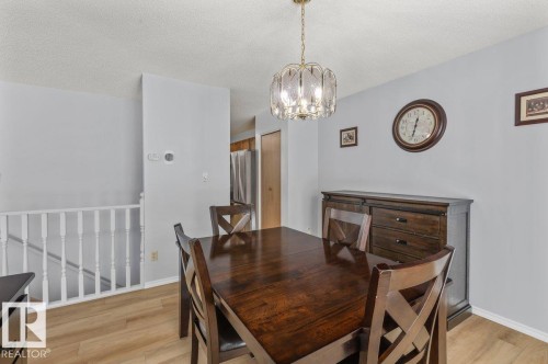 Dining area featuring wood-finish flooring, a tiered glass and brass chandelier, and light gray wall paint - 219 Knottwood Road N, Edmonton, AB - Indoor Photo Showing Dining Room