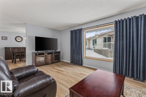 Spacious living area featuring wood-finish flooring, a large picture window with dark drapery, and neutral wall paint - 219 Knottwood Road N, Edmonton, AB - Indoor Photo Showing Living Room