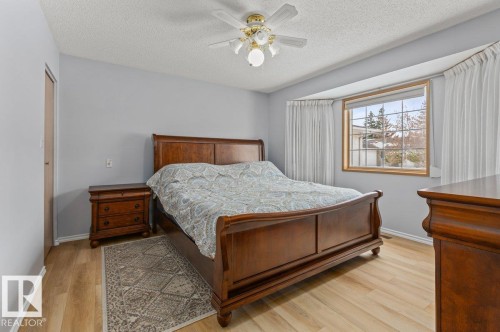 Spacious room featuring light wood-finish flooring, a bay window with a natural wood frame, a ceiling fan with integrated lighting, and neutral wall tones - 219 Knottwood Road N, Edmonton, AB - Indoor Photo Showing Bedroom