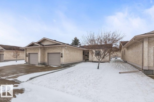 Exterior featuring neutral stucco siding, brown asphalt shingle roofing, and a two-car attached garage with individual doors - 219 Knottwood Road N, Edmonton, AB - Outdoor