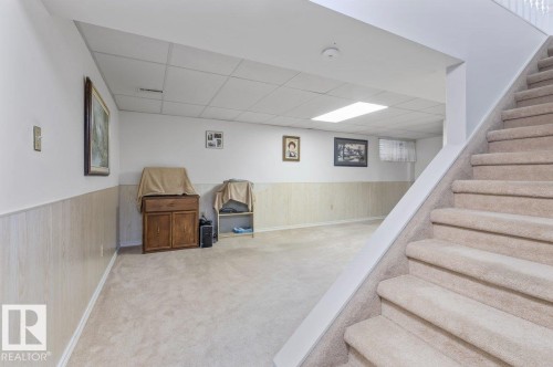 Carpeted staircase descending into a finished lower level with light wood-finish wainscoting and a drop ceiling with recessed lighting - 219 Knottwood Road N, Edmonton, AB - Indoor