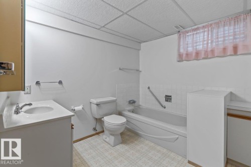 Bathroom featuring a vanity with an integrated sink, a toilet, a bathtub with a grab bar, and patterned vinyl flooring - 219 Knottwood Road N, Edmonton, AB - Indoor Photo Showing Bathroom