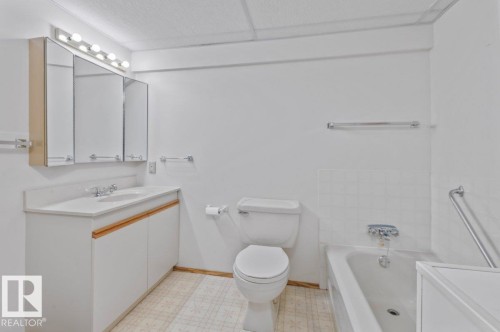 Bathroom featuring a white vanity with a single basin sink, triple mirrored medicine cabinet, overhead vanity lighting, and a white bathtub with subway tile surround - 219 Knottwood Road N, Edmonton, AB - Indoor Photo Showing Bathroom
