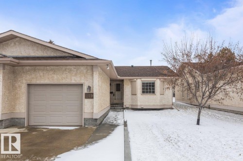 Stucco exterior featuring an attached garage with a panel door, front entry with a storm door, and a bay window with shutters - 219 Knottwood Road N, Edmonton, AB - Outdoor