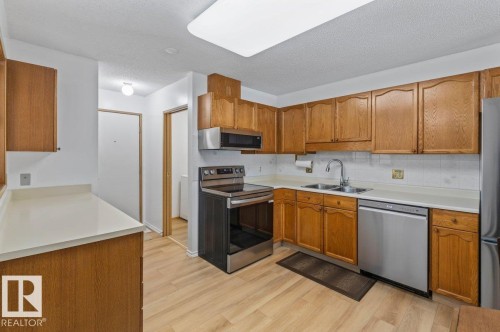 Kitchen featuring wood cabinetry, light-toned countertops, and wood-finish flooring - 219 Knottwood Road N, Edmonton, AB - Indoor Photo Showing Kitchen With Double Sink