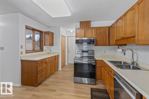 Well-appointed kitchen featuring wood-finish cabinetry, light countertops, stainless steel appliances, and wood-finish flooring - 219 Knottwood Road N, Edmonton, AB - Indoor Photo Showing Kitchen With Double Sink