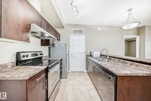 The kitchen features rich wood cabinetry, stainless steel appliances, and durable speckled countertops - 411 6925 199 Street Nw, Edmonton, AB - Indoor Photo Showing Kitchen With Double Sink With Upgraded Kitchen