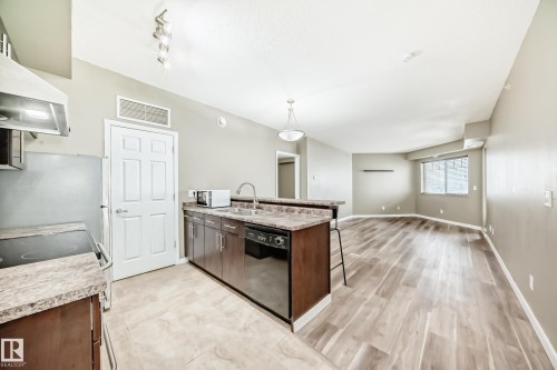 The property features a kitchen with dark cabinetry, stone-look countertops, and stainless steel appliances - 411 6925 199 Street Nw, Edmonton, AB - Indoor Photo Showing Kitchen