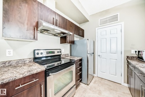 The kitchen features dark wood cabinetry, stainless steel appliances, and granite-look countertops - 411 6925 199 Street Nw, Edmonton, AB - Indoor Photo Showing Kitchen