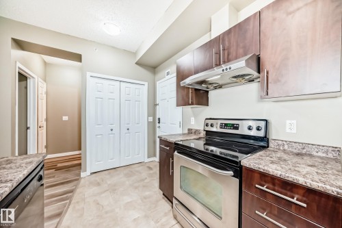 The kitchen features stainless steel appliances, dark wood cabinetry, and speckled countertops - 411 6925 199 Street Nw, Edmonton, AB - Indoor Photo Showing Kitchen