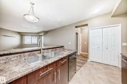 The kitchen features a double stainless steel sink with a high arc faucet, dark wood cabinetry with chrome handles, and a patterned countertop - 