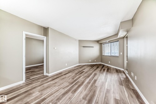 Spacious interior room featuring light-toned walls, wood-style flooring, a window with horizontal blinds, and white trim throughout - 411 6925 199 Street Nw, Edmonton, AB - Indoor Photo Showing Other Room