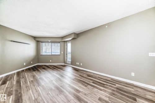 Spacious room featuring wood-look flooring, light-colored walls, a window with horizontal blinds, and a glass-paneled door - 411 6925 199 Street Nw, Edmonton, AB - Indoor Photo Showing Other Room