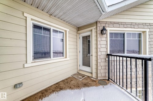 The property features light-colored siding, a white-framed window, and an exterior door leading to a balcony with black railings - 411 6925 199 Street Nw, Edmonton, AB - Outdoor With Exterior