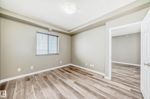 The room features wood-look flooring, light-colored walls, and a window with blinds - 411 6925 199 Street Nw, Edmonton, AB - Indoor Photo Showing Other Room