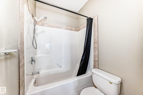 Bathroom featuring a white bathtub and shower combination with a handheld showerhead and a tiled surround - 411 6925 199 Street Nw, Edmonton, AB - Indoor Photo Showing Bathroom
