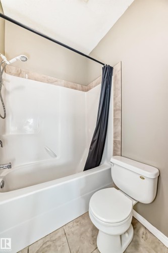 The bathroom features a white bathtub with a shower head, light-toned wall tiling, and a toilet - 411 6925 199 Street Nw, Edmonton, AB - Indoor Photo Showing Bathroom