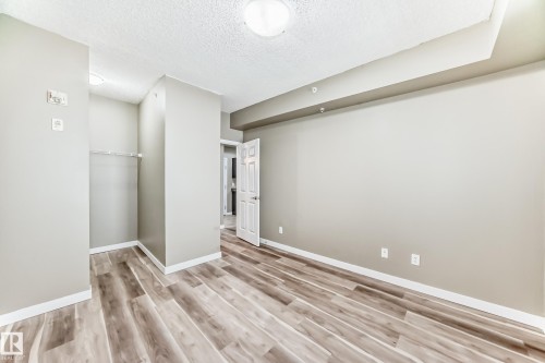 This room features wood-look flooring, light-toned walls, and a recessed ceiling detail - 411 6925 199 Street Nw, Edmonton, AB - Indoor Photo Showing Other Room