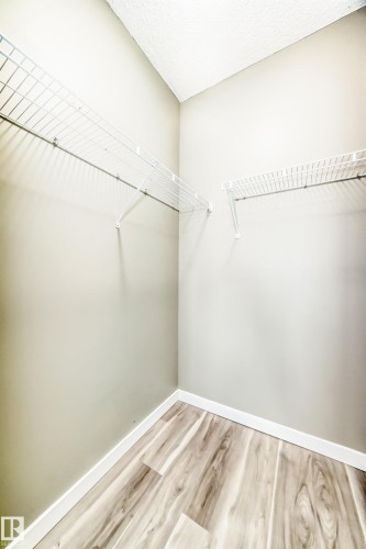 This closet features wire shelving, light-toned walls, and wood-look flooring with white baseboards - 411 6925 199 Street Nw, Edmonton, AB - Indoor With Storage