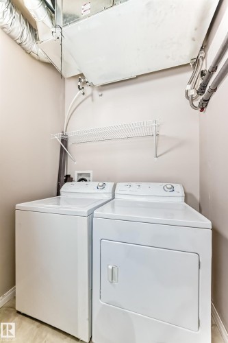 Dedicated laundry area featuring a washer and dryer, an overhead wire shelf, and exposed ductwork - 411 6925 199 Street Nw, Edmonton, AB - Indoor Photo Showing Laundry Room