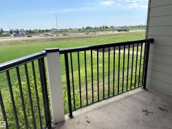 Private balcony featuring a concrete surface, black metal railing, and a distant highway visible over green fields - 