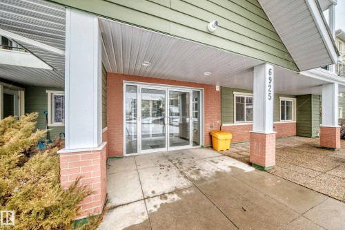The property features an entrance with glass doors, brick detailing, and a prominent address number on a column - 411 6925 199 Street Nw, Edmonton, AB - Outdoor