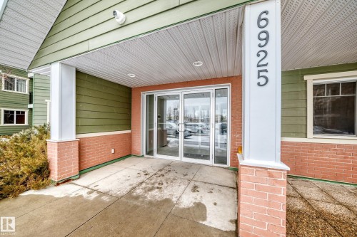 The property features a welcoming entrance with large glass doors, brick detailing, and a prominent address display - 411 6925 199 Street Nw, Edmonton, AB - Outdoor With Exterior