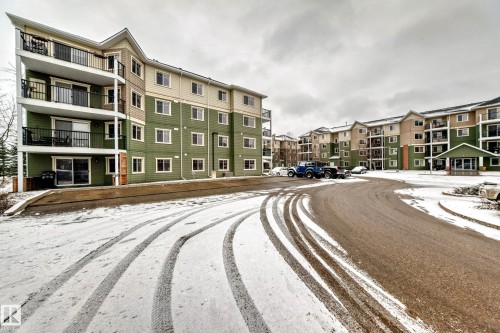 The property features a multi-story building with balconies, visible parking areas, and a paved road - 411 6925 199 Street Nw, Edmonton, AB - Outdoor With Balcony With Facade