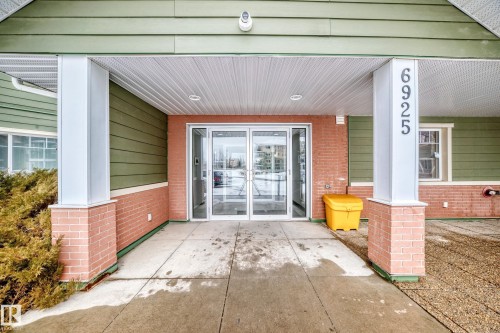 The property features an entrance with automatic sliding doors, brick accents, and a covered porch - 411 6925 199 Street Nw, Edmonton, AB - Outdoor